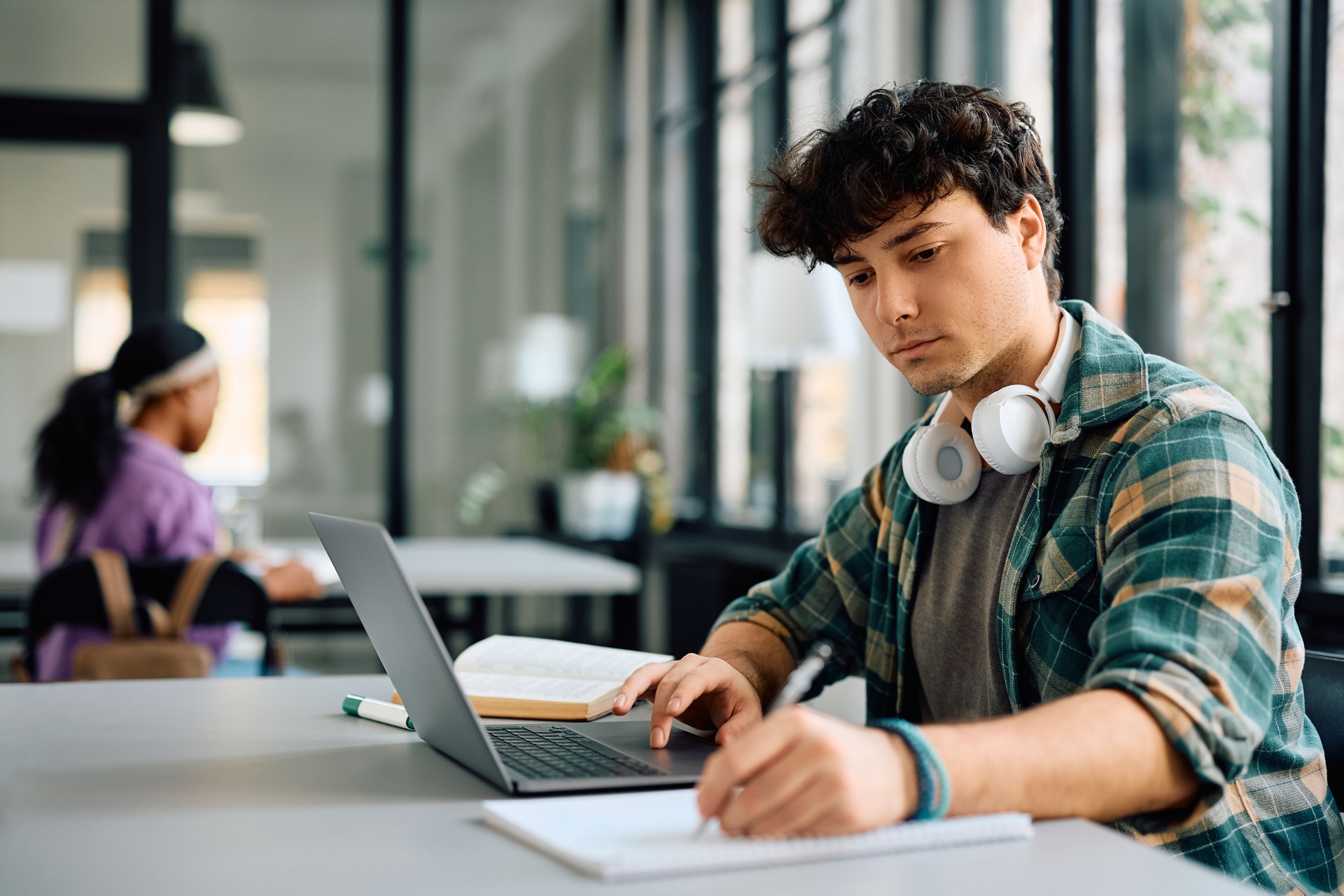 Joven estudiante tomando notas mientras aprende en línea en una computadora portátil en la universidad.